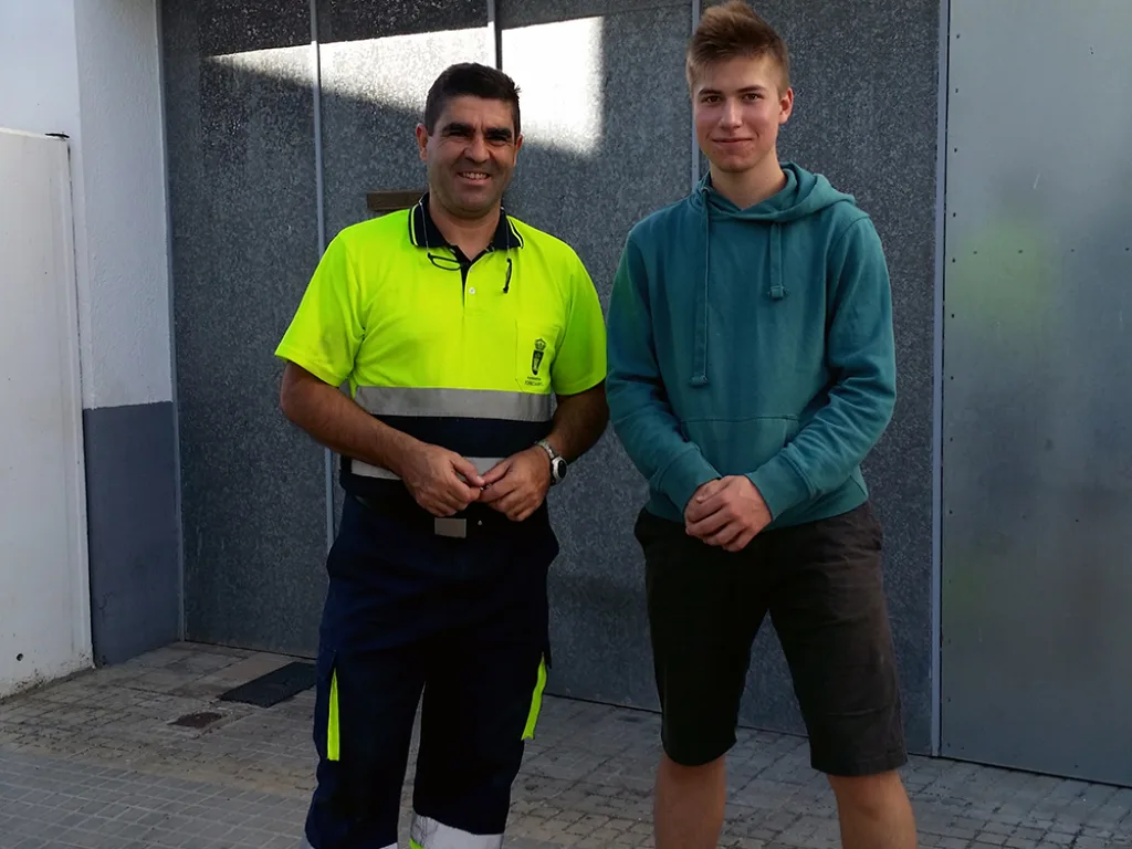 Ein Jugendlicher steht mit einem Mitarbeiter in Warnkleidung vor einem Gebäude.